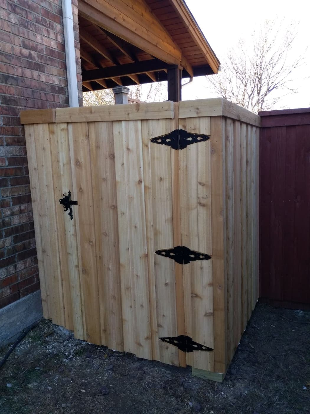 Cedar gate in a brick alcove — three black hinges, black latch