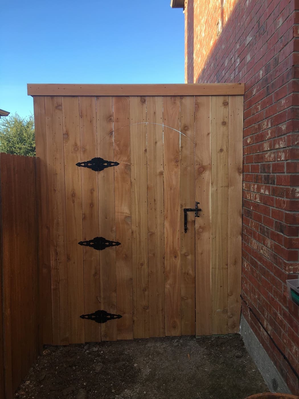 Cedar gate with three black hinges against a brick wall