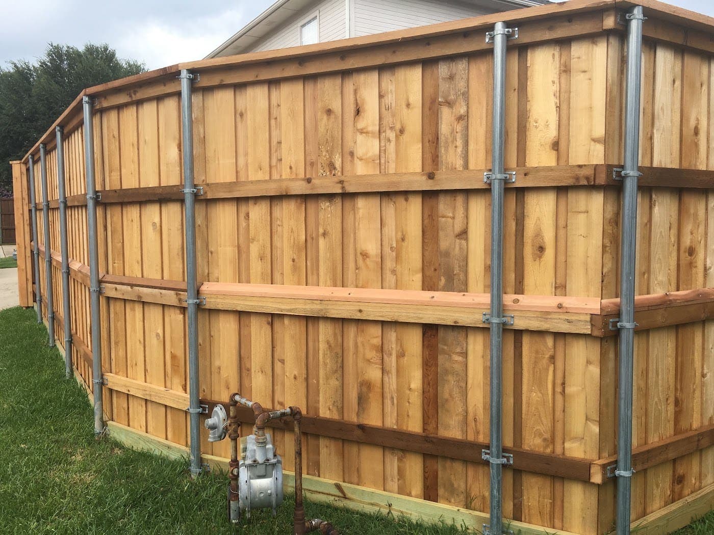 Fence mid-install — steel posts and three cedar rails before pickets